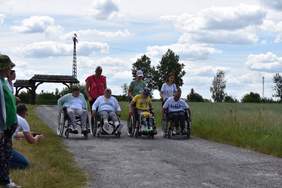 Pokaż zdjęcie: cztery osoby na wózkach inwalidzkich ścigają się, za nimi idą osoby do pomocy