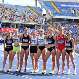 Zawodniczki w rzędzie stoją na bieżni lekkoatletycznej pozując do zdjęcia. Trzymają się przyjaźnie w pasie. 