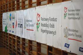 Pokaż zdjęcie: Banery sponsorów wydarzenia zawieszona na drabinach sportowych. Widzimy logo PFRON, Klubu Sportowego Start i Ministerstwa Sportu i Rekreacji