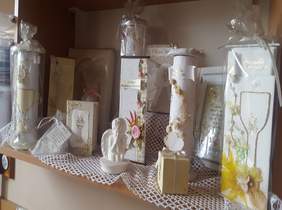 Pokaż zdjęcie: na zdjęciu zamieszczono pamiątki okolicznościowe na komunię tj. białe świece , aniołki oraz zaproszenia wykonane przez uczestników WTZ w Wieruszowie   