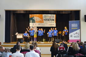 Występ sceniczny 9 osób w niebieskich koszulkach, kobiety i męzczyżni