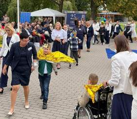 Zdjęcie przedstawia uczestników uroczystości 25-lecia Ośrodka Rehabilitacyjno-Edukacyjno-Wychowawczego w Nowielinie. Na pierwszym planie dzieci i opiekunowie przemieszczają się alejką, a w tle zgromadzeni goście, namiot oraz dekoracje jubileuszowe.