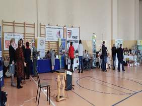 Pokaż zdjęcie: sala gimnanstyczna w tle umieszczono stoiska instytucji o organizacji ze swoimi produktami. Po sali przemieszczają się osoby do stoisk w których prezentowane są oferty instytucji