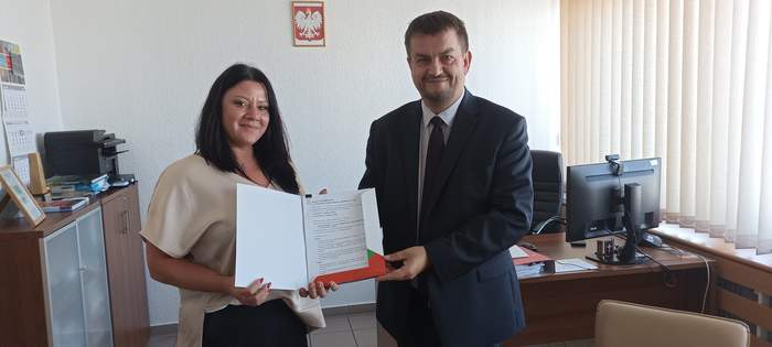 Pokaż zdjęcie: Mężczyzna i kobieta stoją obok siebie i trzymają w ręku umowę, oboje są ubrani na galowo i uśmiechnięci