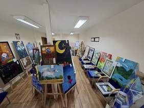 Przestronna sala. Wzdłuż ścian rozmieszczono wiele obrazów na sztalugach, krzesłach.