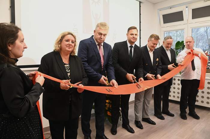 Pokaż zdjęcie: Pięć osób przecina czerwoną wstęgę w nowym budynku PSONI Świdnik.