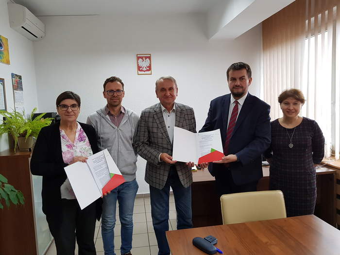 Pokaż zdjęcie: Obok siebie stoją w Gabinecie Dyrektora Oddziału osoby podpisujące umowę, w ręku trzymają egzemplarze umów