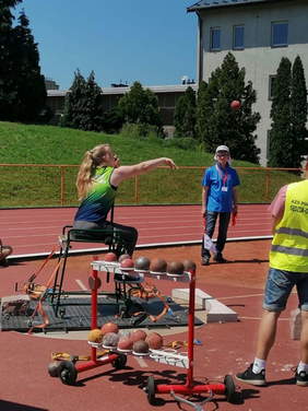 Pokaż zdjęcie: Zawodniczka w trakcie pchnięcia kulą podczas zawodów na tle stadionu