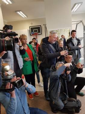 Pokaż zdjęcie: na zdjęciu grupa dziennikarzy trzmająca kamery oraz obiektywy relacjonuje wydarzenie w Fundacji Kolorowy Świat dotyczące zakupu nowego urządzenia do rehabilitacji  