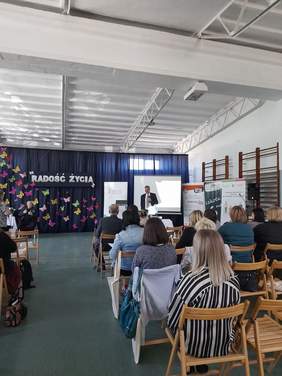 Pokaż zdjęcie: Widok z tyłu sali konferencyjnej w kierunku prelegenta. Na krzesełkach siedzą zaproszeni goście.