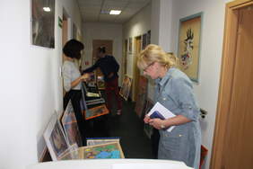 Pokaż zdjęcie: Zdjęcie korytarza biurowego, na krzesłach i podłodze poustawiane są prace plastyczne, komisja plastyczna przygląda się pracom, w skład komisji wchodzą trzy kobiety i mężczyzna