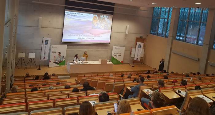 Pokaż zdjęcie: Sala wykładowa wraz z uczestnikami konferencji. Na dole sali można dostrzec trzy osoby, z czego jedna przemawia do mikrofonu. W tle widoczny jest duży ekran, na którym wyświetlona jest prezentacja. Po obu stronach ekranu ustawione są banery PFRON.