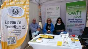 Pokaż zdjęcie: Na Rynku łódzkiej Manufaktury znajduje się stoisko Centrum Informacyjno-Doradczego dla Osób z Niepełnosprawnościami Łódzkiego Oddziału PFRON oraz Ośrodka Wsparcia i Testów w Łodzi. Przy stoisku siedzą trzy osoby: dwie kobiety i mężczyzna. 