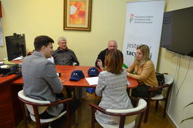 Pokaż zdjęcie: Na zdjęciu 2 kobiety i mężczyzna. Jedna z kobiet trzyma teczkę z logo PFRON. Wszyscy się uśmiechają