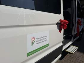 Pokaż zdjęcie: Zbliżenie na drzwi busa, na których widnieje naklejka, iż bus jest dofinansowny ze środków PFRON
