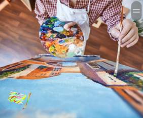 Pokaż zdjęcie: Człowiek trzyma w dłoni kolorową paletę z farbami. W drugiej dłoni trzyma pędzel i maluje obraz. W lewym dolnym rogu umieszczone jest logo przeglądu oraz jego nazwa: "Sztuka jak balsam". 