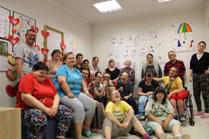 Pokaż zdjęcie: Osoby z niepełnosprawnością zgromadzone w jednym pomieszczeniu, są uśmiechnięci, ubrani na kolorowo