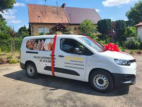 Pokaż zdjęcie: Samocjód elektryczny z uroczystą czerwoną wstążką przed siedzibą spółdzielni