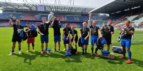 Pokaż zdjęcie: 10 zawodników zwycięskiej drużyny Wataha Bytom. Zawodnicy są na murawie Stadionu Wisły, podskakują, wiwatują. W rękach trzymają nagrody, na szyjach mają złote medale. Jeden zawodnik podnosi ogromny puchar. 