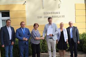 Pokaż zdjęcie: Zdjęcie pozowane przed budynkiem. Przewodnicząca PSONI koło w Nidzicy Ewa Gałka ściska dłoń dyrektora PFRON Mateusza Szkaradzińskiego