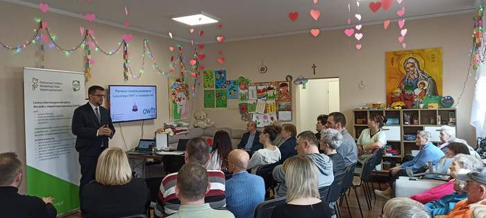 Pokaż zdjęcie: Dyrektor Oddziału przemawia w siedzibie Ośrodka na tle prezentacji, obok zgromadzeni goście