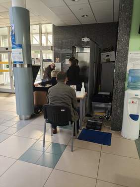 Pokaż zdjęcie: Przy biurku siedzą dwie osoby, które rozmawiają, obok biurka stoi analizator składu ciała.