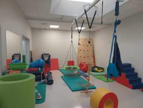 Pokaż zdjęcie: W sali do zajęć z integracji sensorycznej znajdują się różne huśtawki, ścianka wspinaczkowa, maty, podnośniki. Wnętrze jest bardzo kolorowe i przytulne. 