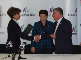 Pokaż zdjęcie: Marlena Maląg, Prezes Zarządu PFRON podpisuje Partnerstwo dla osób z niepełnosprawnościami z Witoldem Kozłowskim, Marszałkiem woj.małopolskiego w obecności Premier Beaty Szydło.
