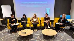 Pokaż zdjęcie: Sala konferencyjna, na środku na żółtych fotelach siedzi 5 kobiet - panelistek