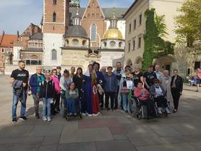 Pokaż zdjęcie: Na tle Katedry na Wawelu stoi grupa ponad 20 osobowa w tym 3 osoby są na wózkach inwalidzkich 