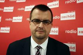 Pokaż zdjęcie: Dyrektor Oddziału Lubuskiego PFRON na tle ścianki promocyjnej Radia Zachód. Ścianka jest w kolorze czerwonym, z białymi napisami Radio Zachód, a Dyrektor jest ubrany w garnitur z krawatem