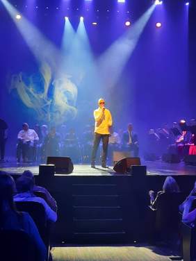 Pokaż zdjęcie: Na scenie stoi Krzysztof Krawczyk junior. Trzyma w dłoniach mikrofon i śpiewa piosenkę. 