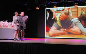 Pokaż zdjęcie: Po lewej stronie kobieta i mężczyzna w średnim wieku odczytują tekst z karki przy mikrofonie, po prawej prezentacja z działalności koła