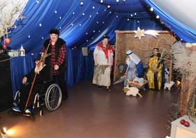 Pokaż zdjęcie: Na scenie wystawiane są jasełka przez osoby z niepełnosprawnościami. Aktorzy są pięknie poprzebierani. Stoi żłóbek, zwierzęta i inne dekoracje. 