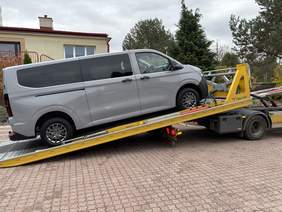 Pokaż zdjęcie: Szary dziewięcioosobowy mikrobus zjeżdża z lawety przed budynkiem Specjalnego Ośrodka Szkolno-Wychowawczego w Długoborzu. Pojazd właśnie został dostarczony do placówki.