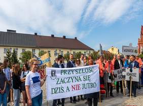 Pokaż zdjęcie: osoby idą z transparentami w stronę parku 