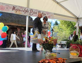 Pokaż zdjęcie: Na scenie stoi mężczyzna i kobieta, mężczyzna trzyma kosz z cukierkami i przemawia do mikrofonu