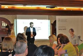 Pokaż zdjęcie: Bartłomiej Kakiet specjalista ds. wdrożeń z Wydziału ds. projektu Systemu Obsługi Wsparcia finansowanego ze środków PFRON na tle ekranu multimedialnego