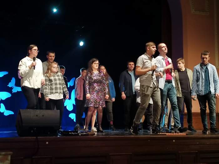 Grupa osób, stoją na scenie z mikrofonami w dłoniach