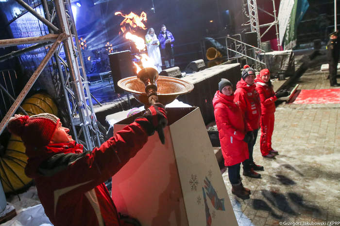 Pokaż zdjęcie: Mężczyzna trzyma w ręku pochodnię z ogniem i zapala znicz olimpijski