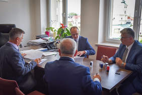 Pokaż zdjęcie: Czterech mężczyzn w pokoju przy stole podpisują dokumenty