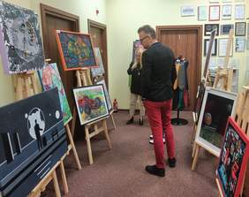 Pokaż zdjęcie: pomieszczenie Oddziału na którym rozmieszczono sztalugi z pracami uczestników po środku czlonkowie komisji oglądają i oceniają prace konkursowe