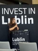 Kobieta przemawia do mikrofonu przy mównicy na tle ścianki z napisem „Invest in Lublin”.