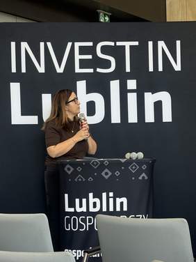 Pokaż zdjęcie: Kobieta przemawia do mikrofonu przy mównicy na tle ścianki z napisem „Invest in Lublin”.