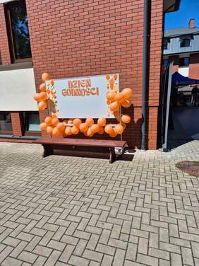 Pokaż zdjęcie: Pomarańczowy napis dzień godności na białym tle, wokół przyczepiono pomarańczowe balony.