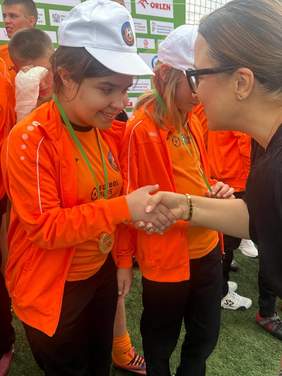 Pokaż zdjęcie: Kobieta pochyla się w kierunku zawodniczki, trzyma ją za rękę i składa gratulacje. 