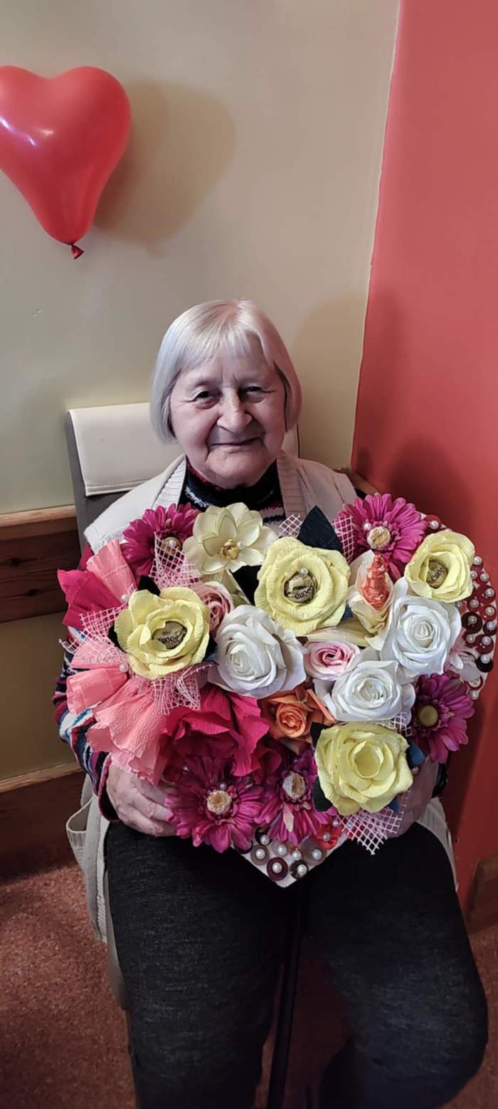 Pokaż zdjęcie: Kobieta w starszym wieku trzyma w dłoniach bukiet kwiatów
