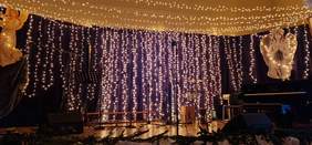 Pokaż zdjęcie: Nastrojowo oświetlona scena z girlandami świateł, mikrofonami i instrumentami, przygotowana do koncertu