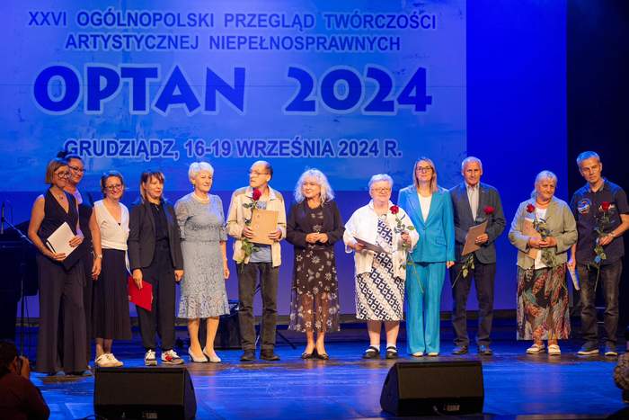 Grupa osób stoi na scenie w świetle reflektorów - laureaci i zaproszeni goście