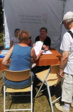 Pokaż zdjęcie: Dwie kobiety trzymające ulotkę w ręku, w tle widać dziecko i mężczyznę – Warszawa.